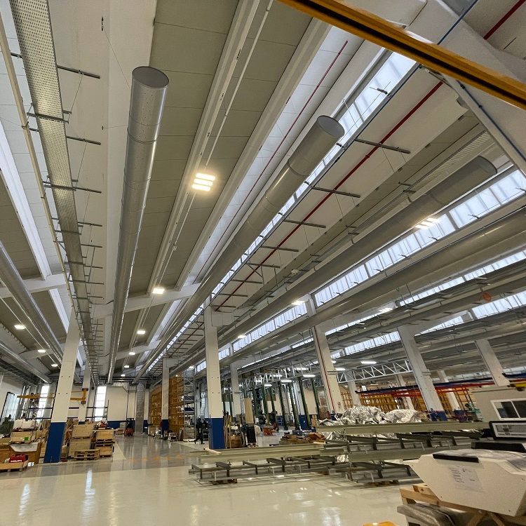 Fabrieksinterieur met wit plafond, steunpilaren, apparatuur en geperforeerde metalen luchtverdeelkanalen