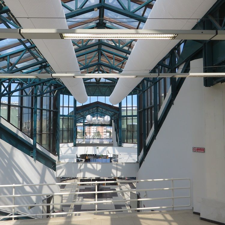 Een architectonisch interieurbeeld van een lichte, lichtrijke structuur met glazen wanden en plafond, een aflopende trap en ronde textiele luchtverdeelslangen & airsocks.