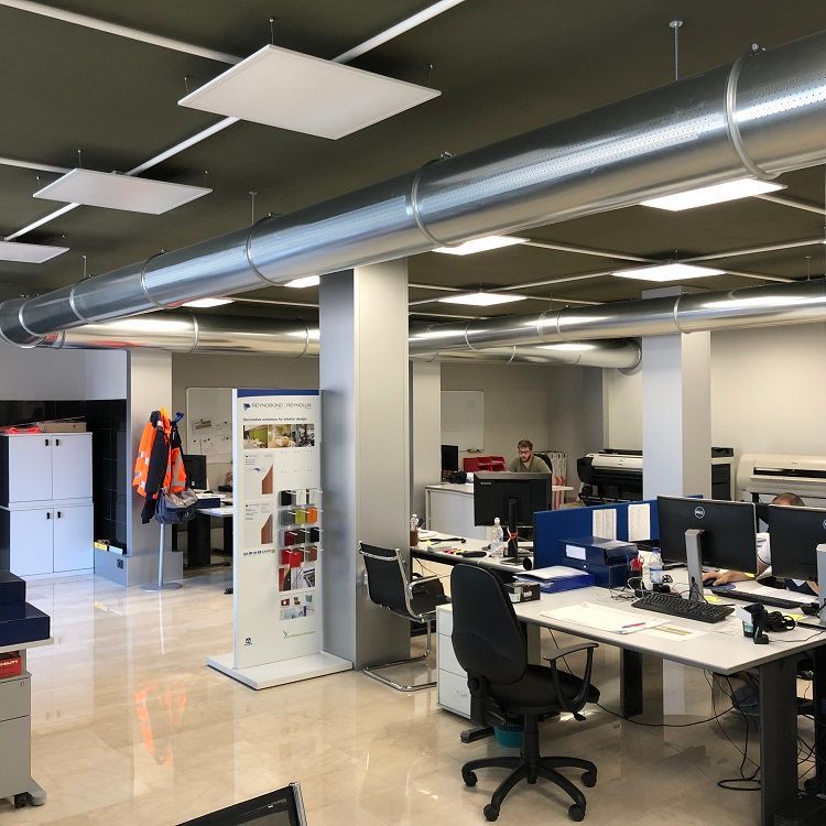 Kantoorruimte met bureaus, computers en medewerkers. Metalen geperforeerde metalen luchtverdeelkanalen voor de verwarming, ventilatie en airconditioning lopen over het plafond.
