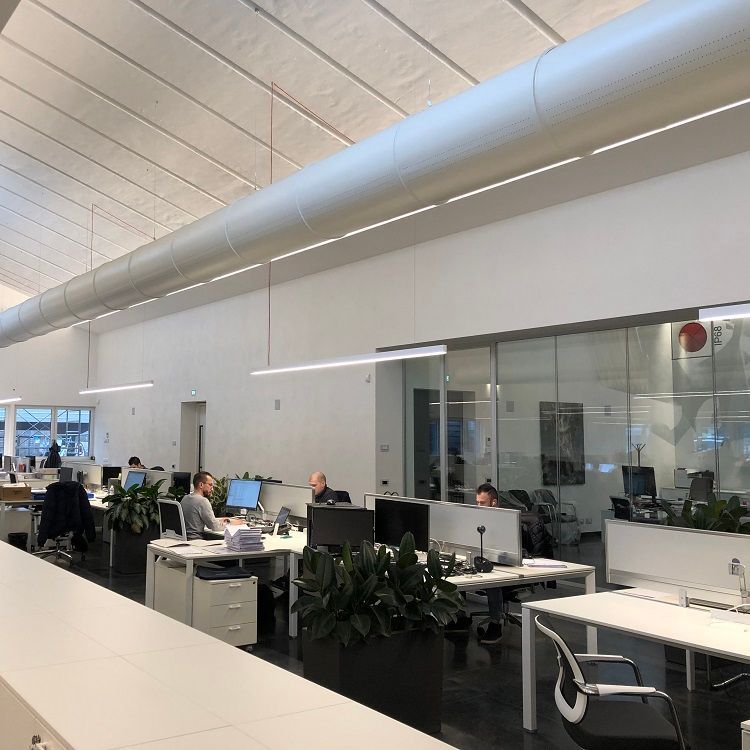 Kantoorinterieur met mensen aan bureaus, witte muren, glazen scheidingswanden en wit gespoten geperforeerde metalen luchtverdeelkanalen