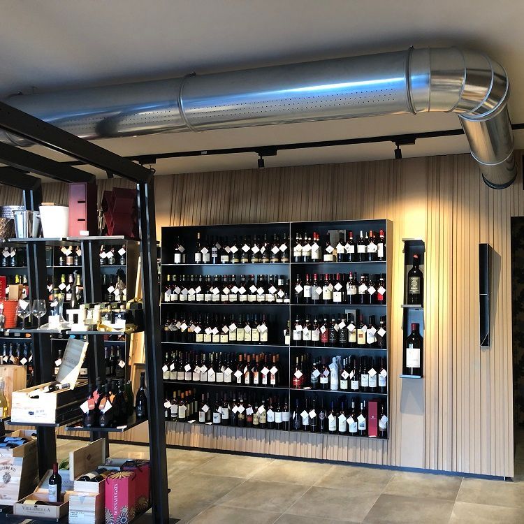 Wijnflessen staan ​​uitgestald op planken in een winkel, een houten lambrisering en  geperforeerde metalen luchttoevoerkanalen.