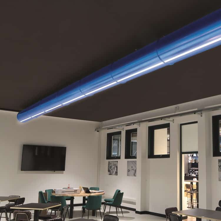 Een blauw geintegreerde verlichte geperforeerd luchtverdeelkanaal in een kamer met een zwart plafond, witte muren en tafels en stoelen.