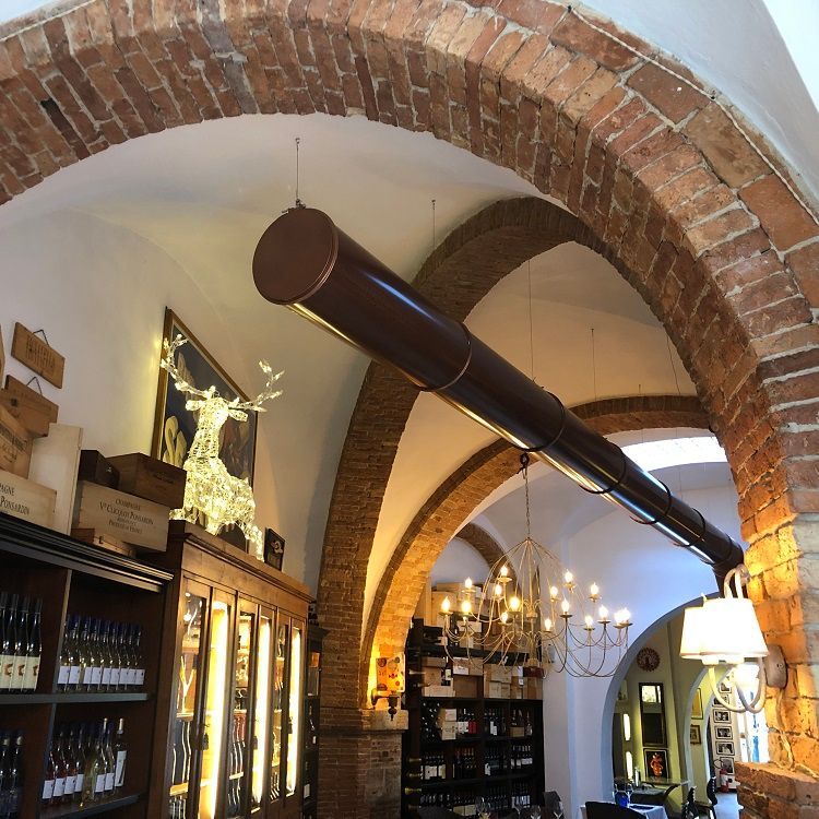 Binnen in een winkel met een bakstenen boog; wijnflessen op de planken, een decoratieve kroonluchter,een hert met verlichting en bruine metalen geperforeerde luchtverdeelkanalen.