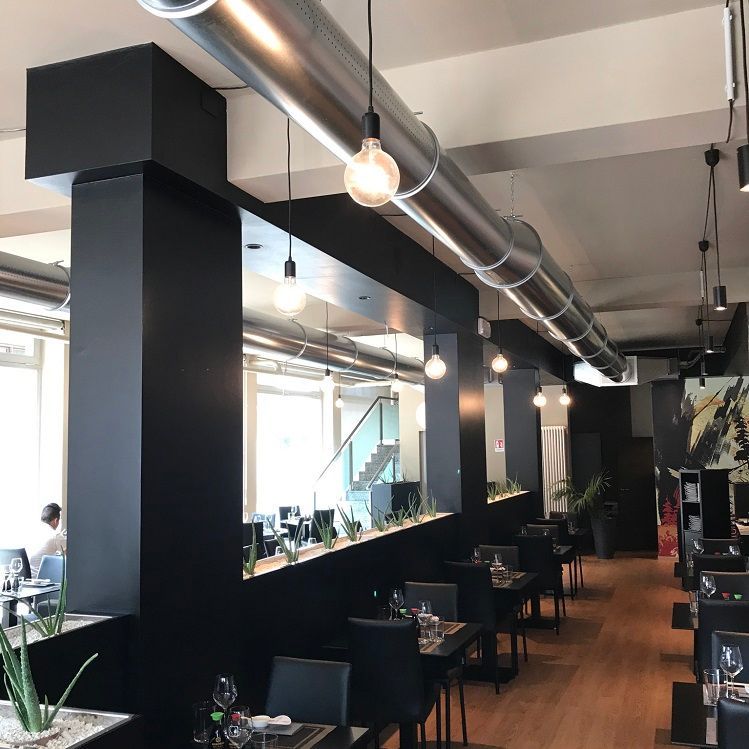 Restaurantinterieur met zwarte pilaren, tafels en een lange, zilverkleurige geperforeerde metalen luchtverdeelkanalen.