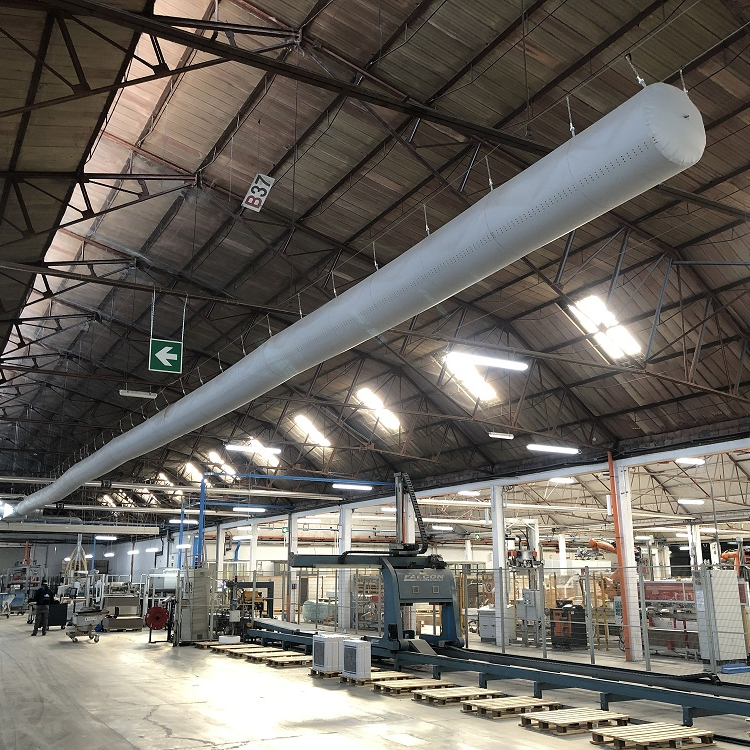 Een lange, cilindrische stoffen airsok hangt aan het plafond van een industriële loods.