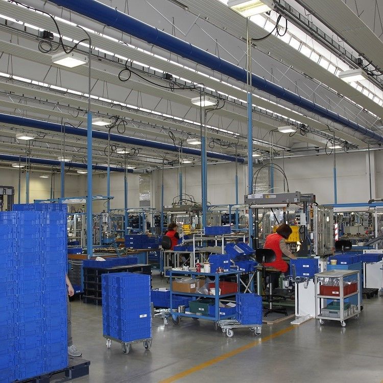 Fabrieksinterieur met machines, arbeiders in rode uniformen, blauwe opslagcontainers en blauwe metalen luchtverdeelkanalen
