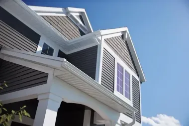 Exterior view of house with dark gray siding, white trim, and gutters against a blue sky.