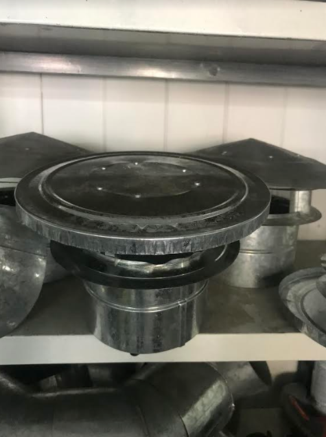 Un utensilio de cocina redondo de color negro o una tapa de olla sobre un estante de metal junto con otros utensilios de cocina.