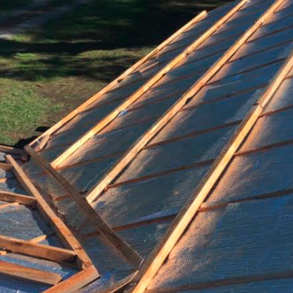 Primer plano de un tejado parcialmente en construcción, con vigas de madera y revestimiento metálico.