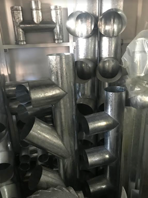 Conductos y accesorios de tubería de metal plateado apilados en un área de almacenamiento.