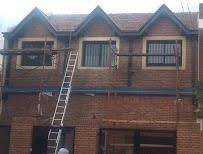 Casa de ladrillo con una escalera apoyada en una ventana del piso superior y trabajadores cerca del tejado.