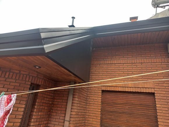 Exterior de una casa de ladrillo con el borde del tejado dañado y un tendedero que cruza la estructura.