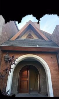 Entrada de capilla de ladrillo con puerta arqueada y techo triangular empinado bajo un cielo nublado.