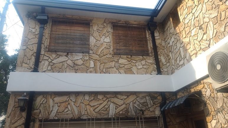 Fachada de edificio de piedra con balcón blanco, contraventanas cerradas y una unidad de aire acondicionado a la derecha.