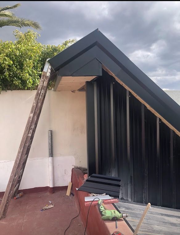 Estructura de azotea parcialmente construida con paneles de techo negros, escalera y herramientas en una terraza.