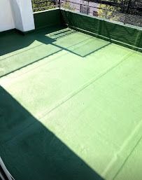 Terraza verde en la azotea con barandilla, luz solar y baldosas en el suelo que crean sombra.