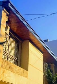 Pared y tejado amarillos de una casa contra un cielo azul, con ventanas y barandilla en el balcón.