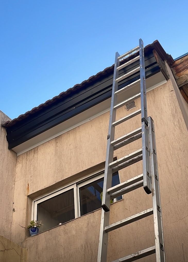 Escalera extensible apoyada contra una casa beige bajo un cielo azul