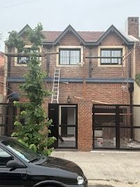 Fachada de ladrillo de una casa adosada con una escalera apoyada contra ella y un coche negro aparcado delante.