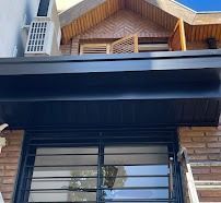 Exterior de la casa con toldo oscuro, paredes de ladrillo y frontón decorativo de madera sobre una ventana.