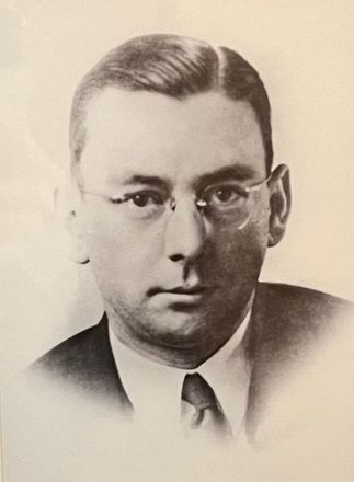 A black and white photo of a man wearing glasses and a suit and tie.