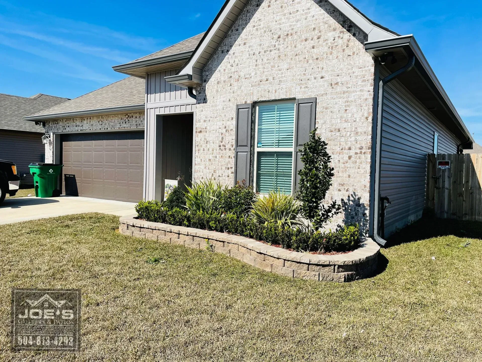 Modern single-story house with stone façade, garage, front entry, and landscaped yard under a clear blue sky