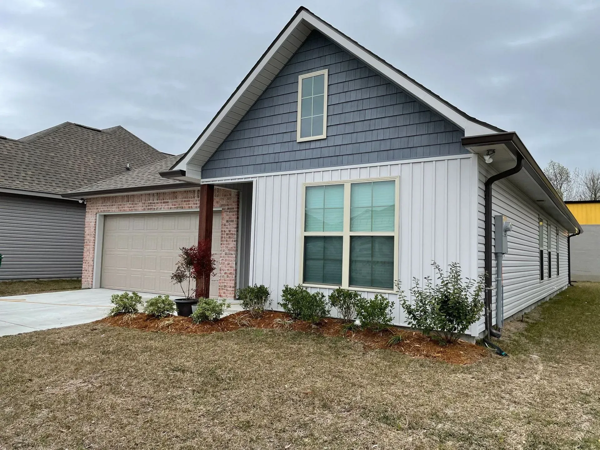 Suburban house with gray siding, white trim, brick facade, and a small front lawn.