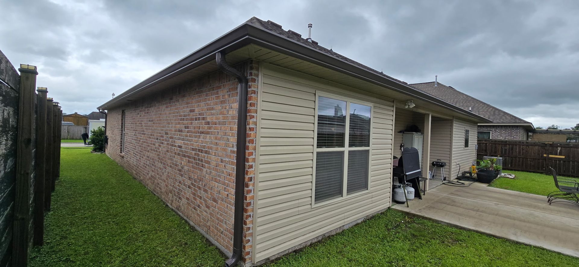Exterior view of the side and front corner of a brick and light-colored siding house with a concrete driveway.