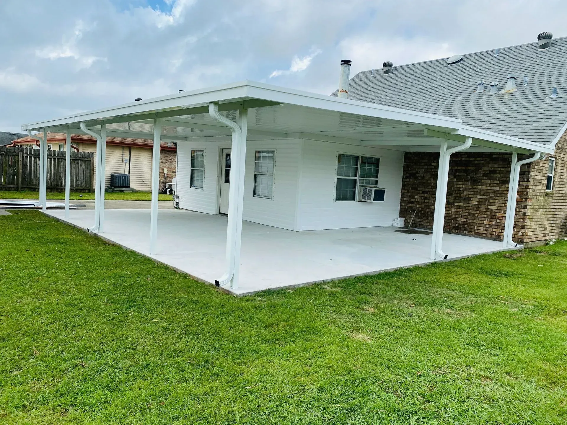 White house with a covered porch and green lawn under a cloudy sky