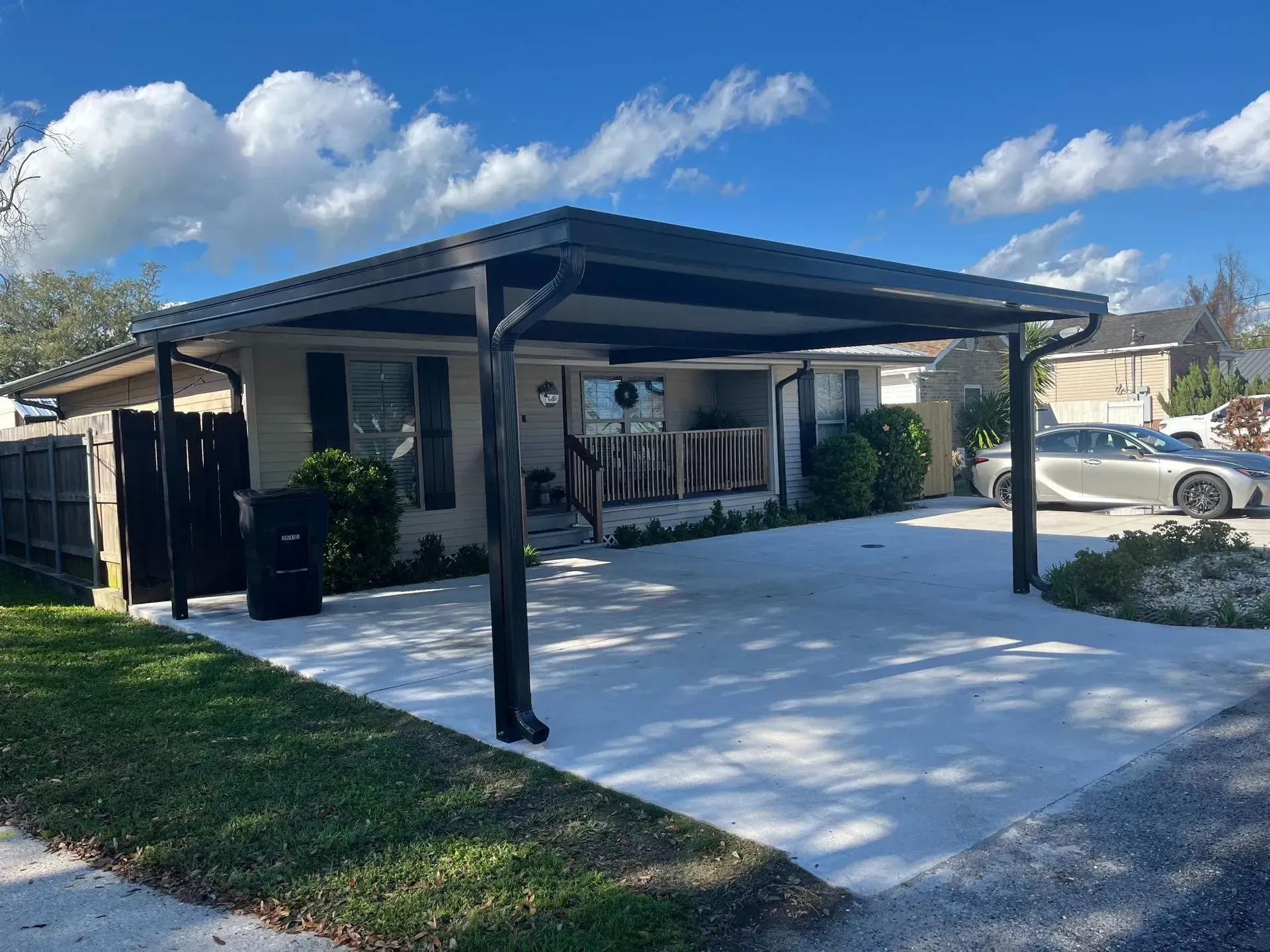 Covered carport beside a house with a white concrete driveway under a blue sky
