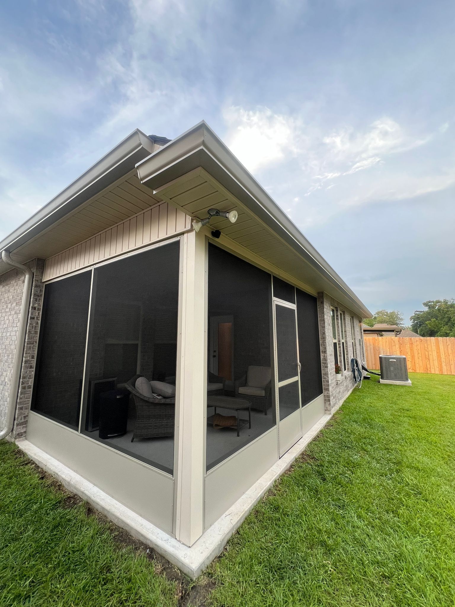 A screened-in porch with light-colored siding and a corner post, overlooking a grassy backyard under a cloudy sky.