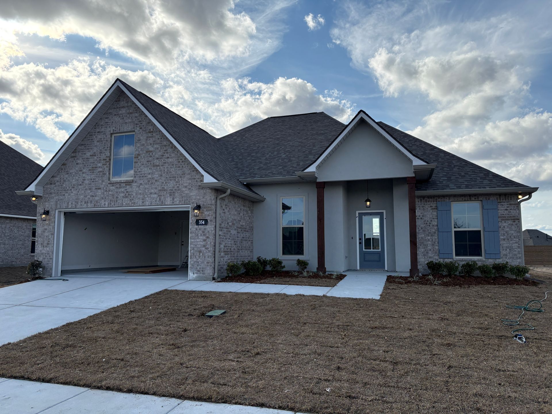 A single-story suburban house with a brick and stucco exterior, an open garage, and a concrete driveway under a cloudy sky.