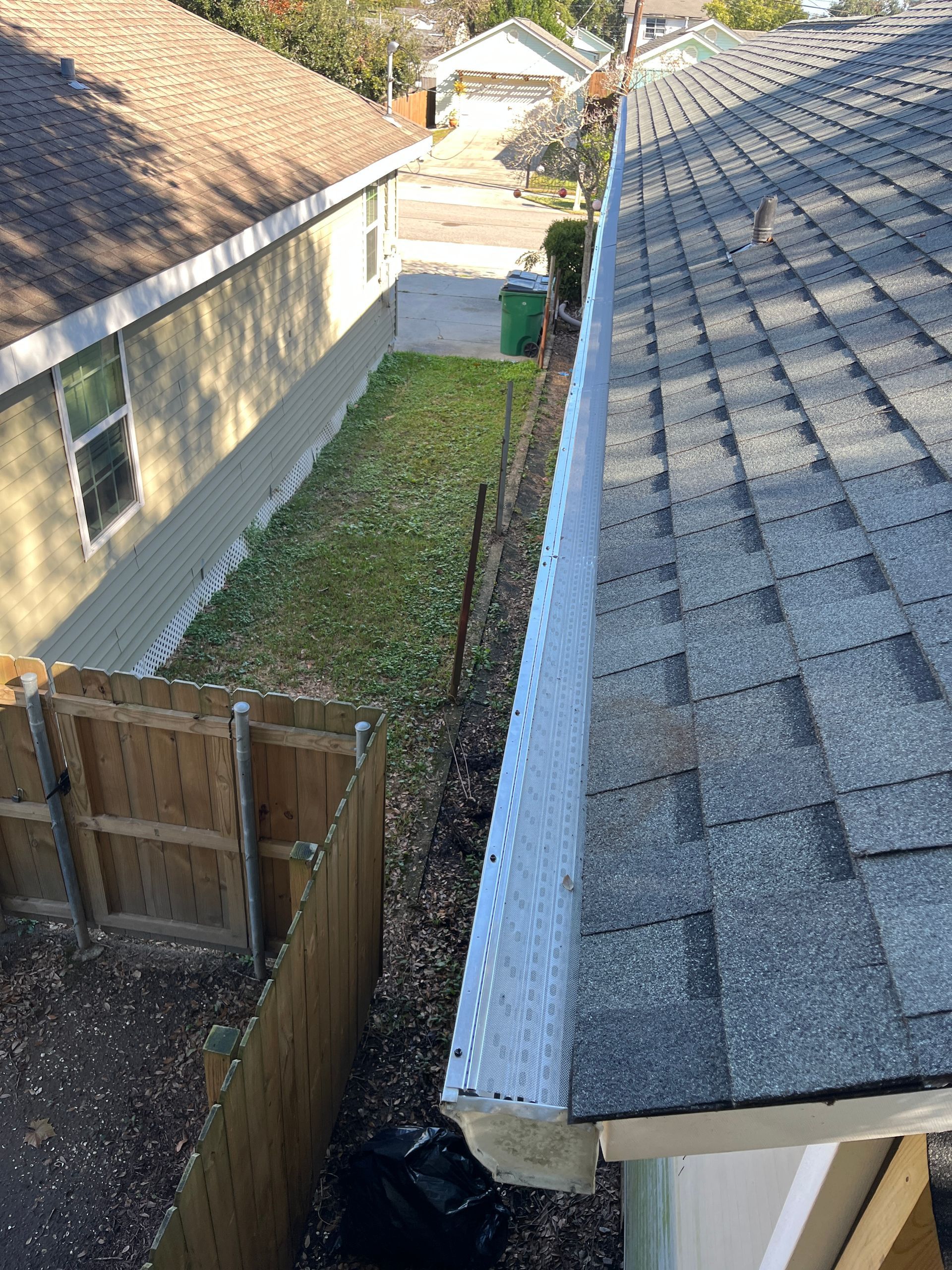 High-angle view of a residential roof edge with a white gutter guard, overlooking a narrow yard and neighboring house.