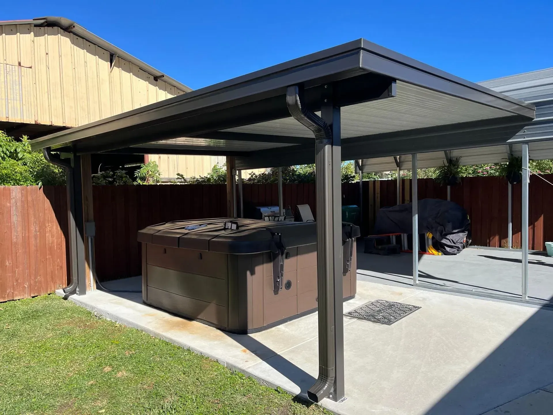 Covered backyard patio with hot tub, concrete floor, and grass yard beside a wooden fence