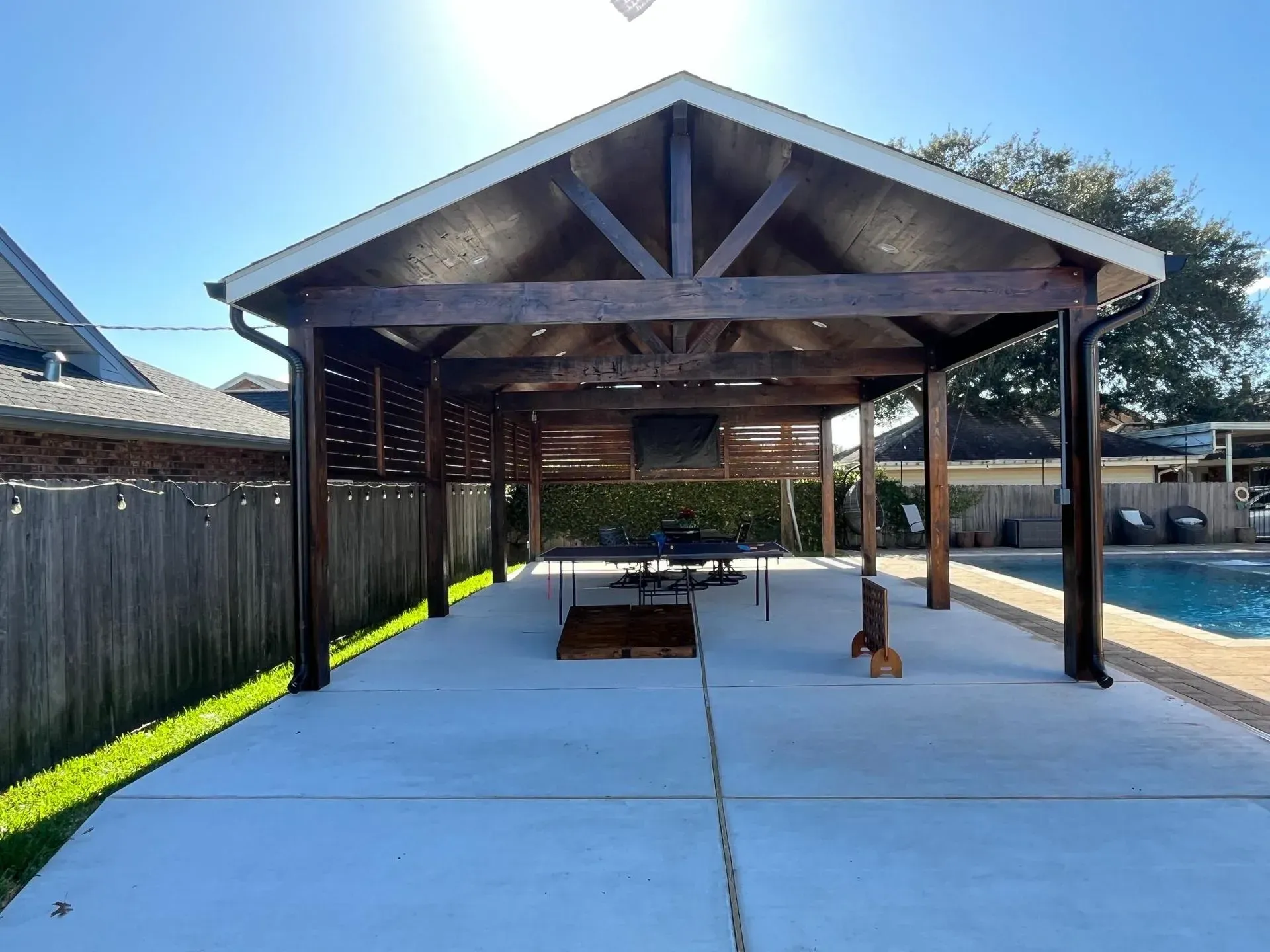 Covered patio with exposed beams, concrete floor, and wooden fence in a backyard.