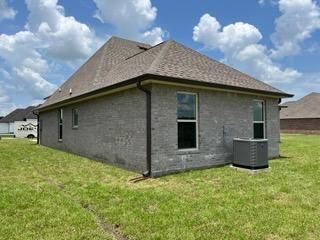 A grey brick single-family house with a brown hip roof, seen from the side yard on a sunny day with a blue sky.