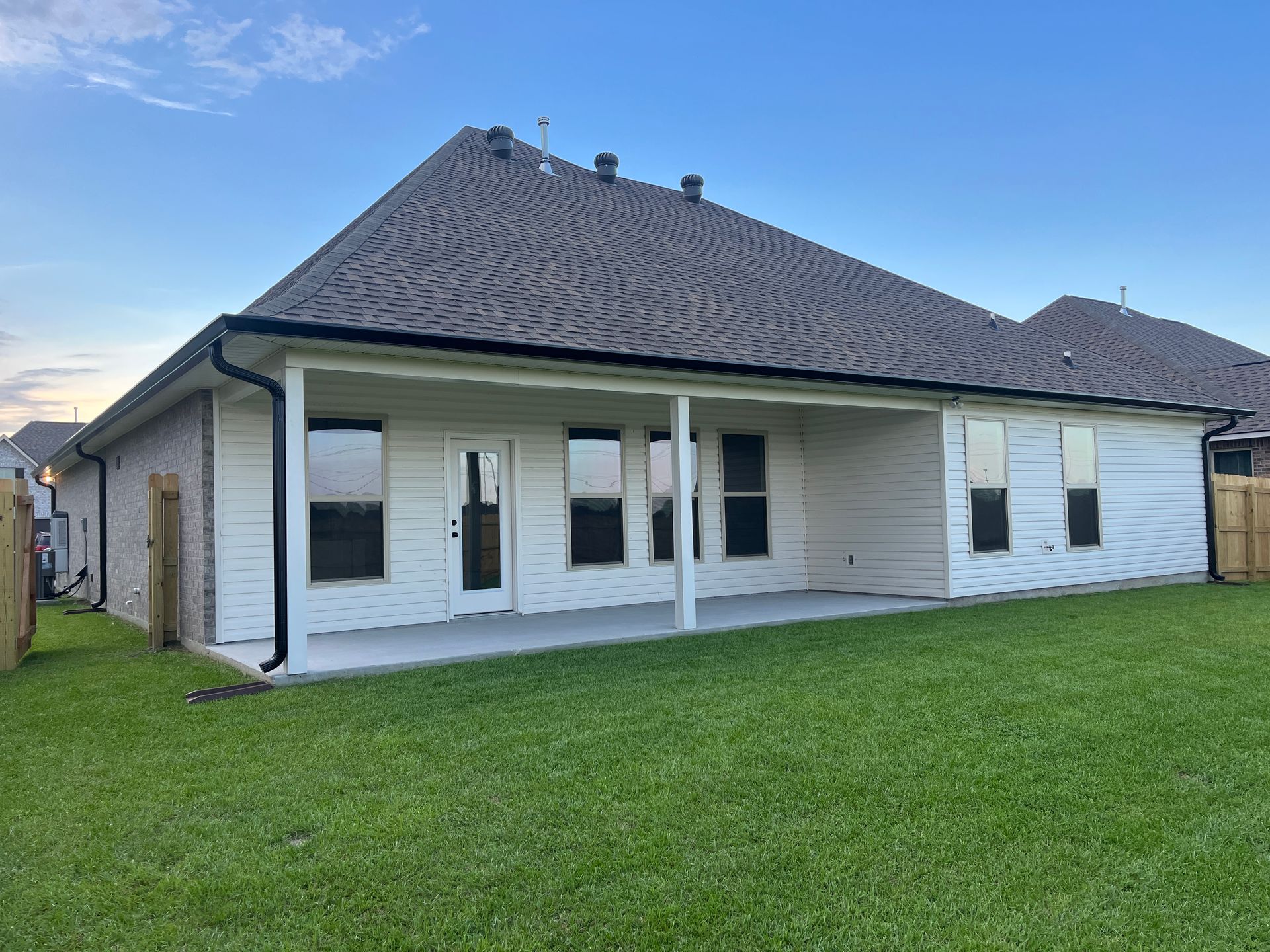 The back exterior of a single-story home with a covered patio, cream-colored siding, dark shingles, and a grassy yard.