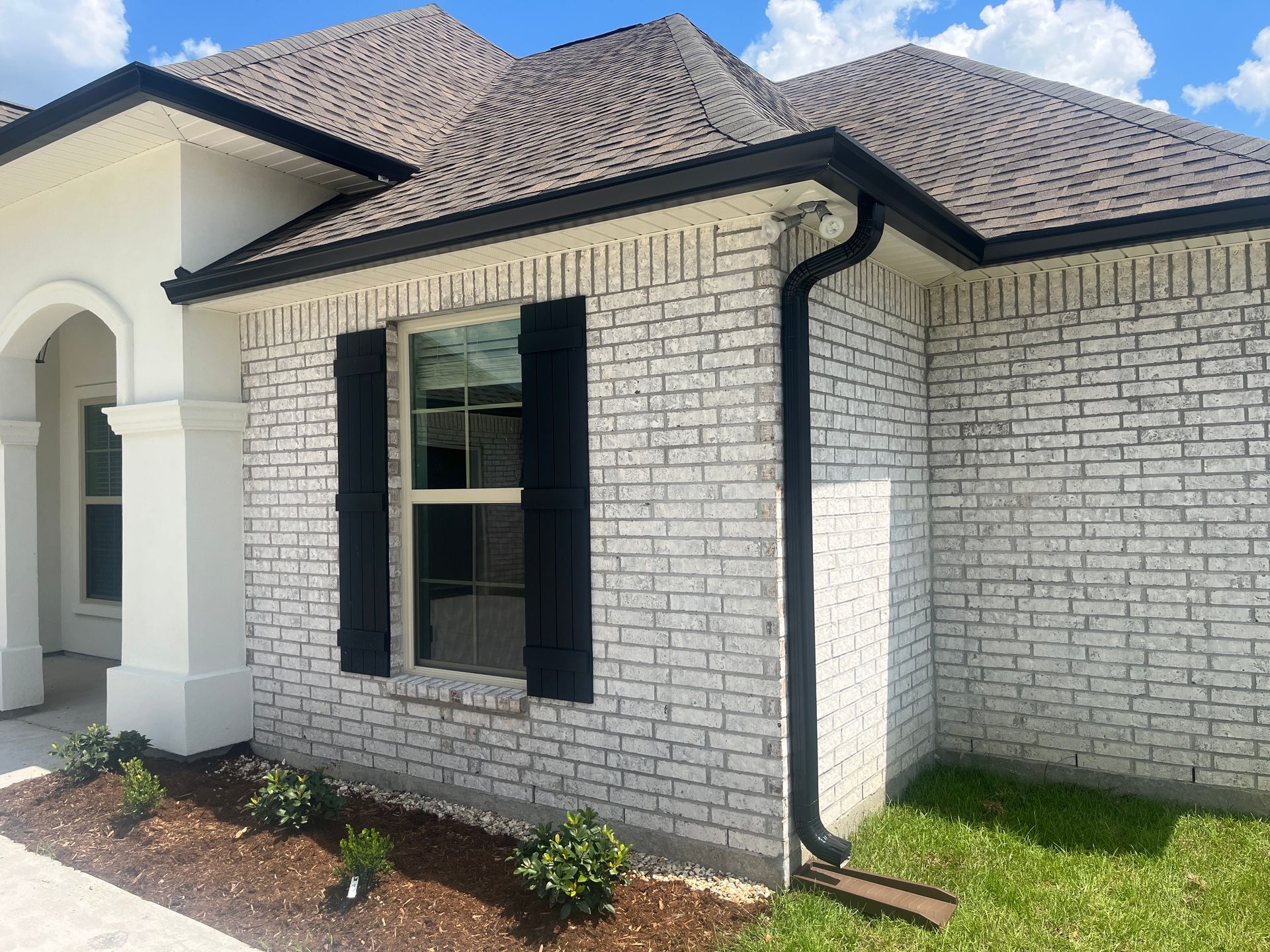 White brick house exterior with black shutters, arched entry, and dark roof trim