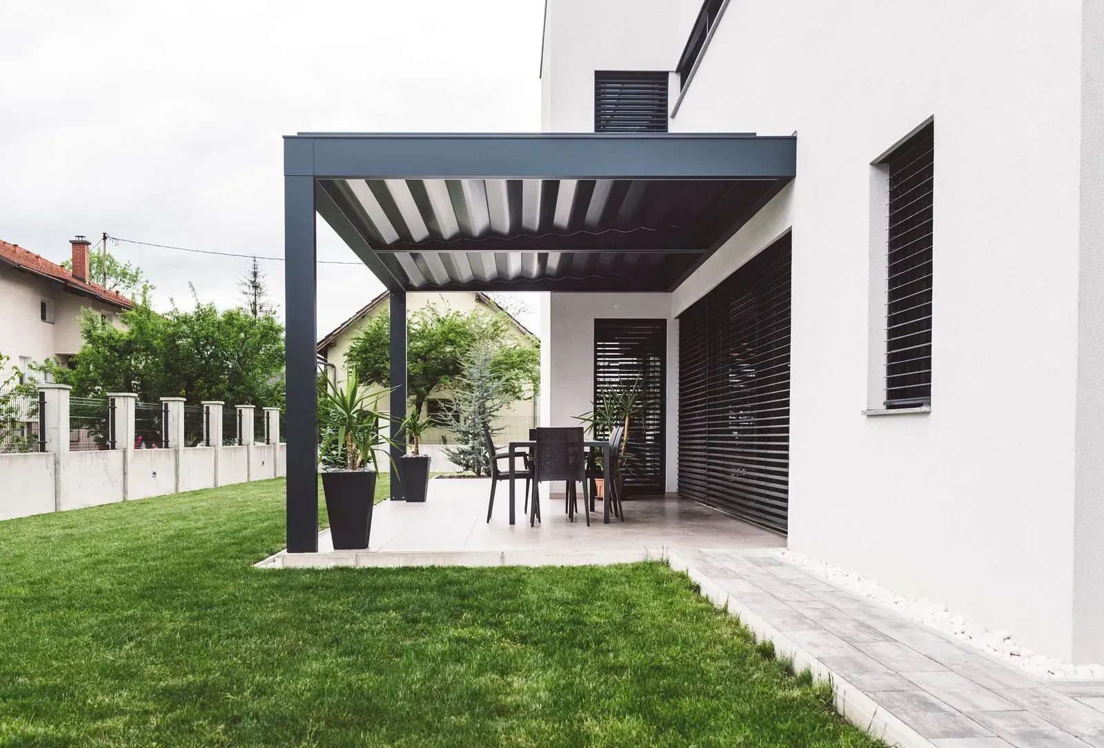 Modern white house patio with dark pergola, outdoor table and chairs, and green lawn