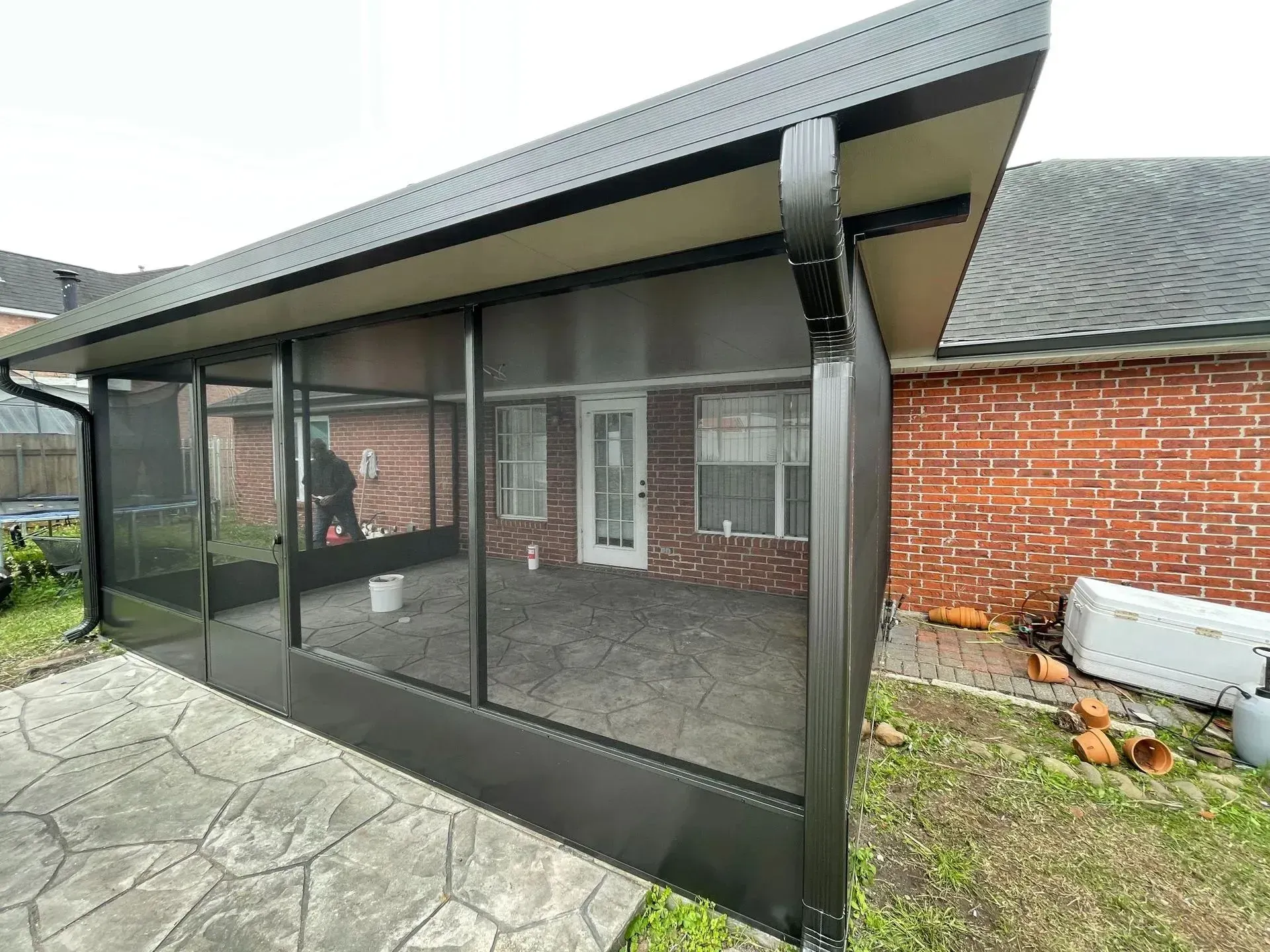 Black screened patio enclosure attached to a brick house beside a stone patio.