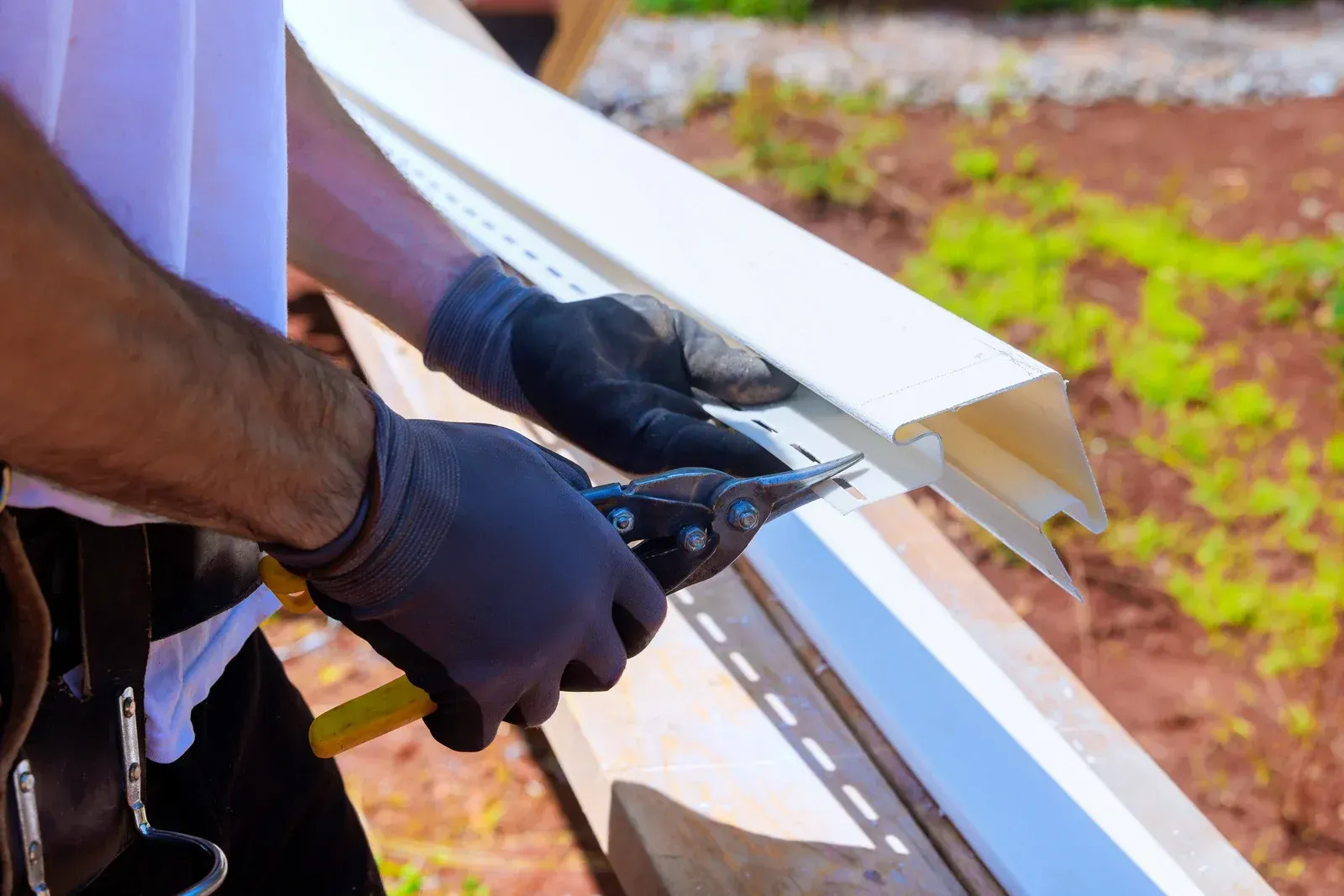 Hand holding black gutter downspout under roof eave on a house exterior