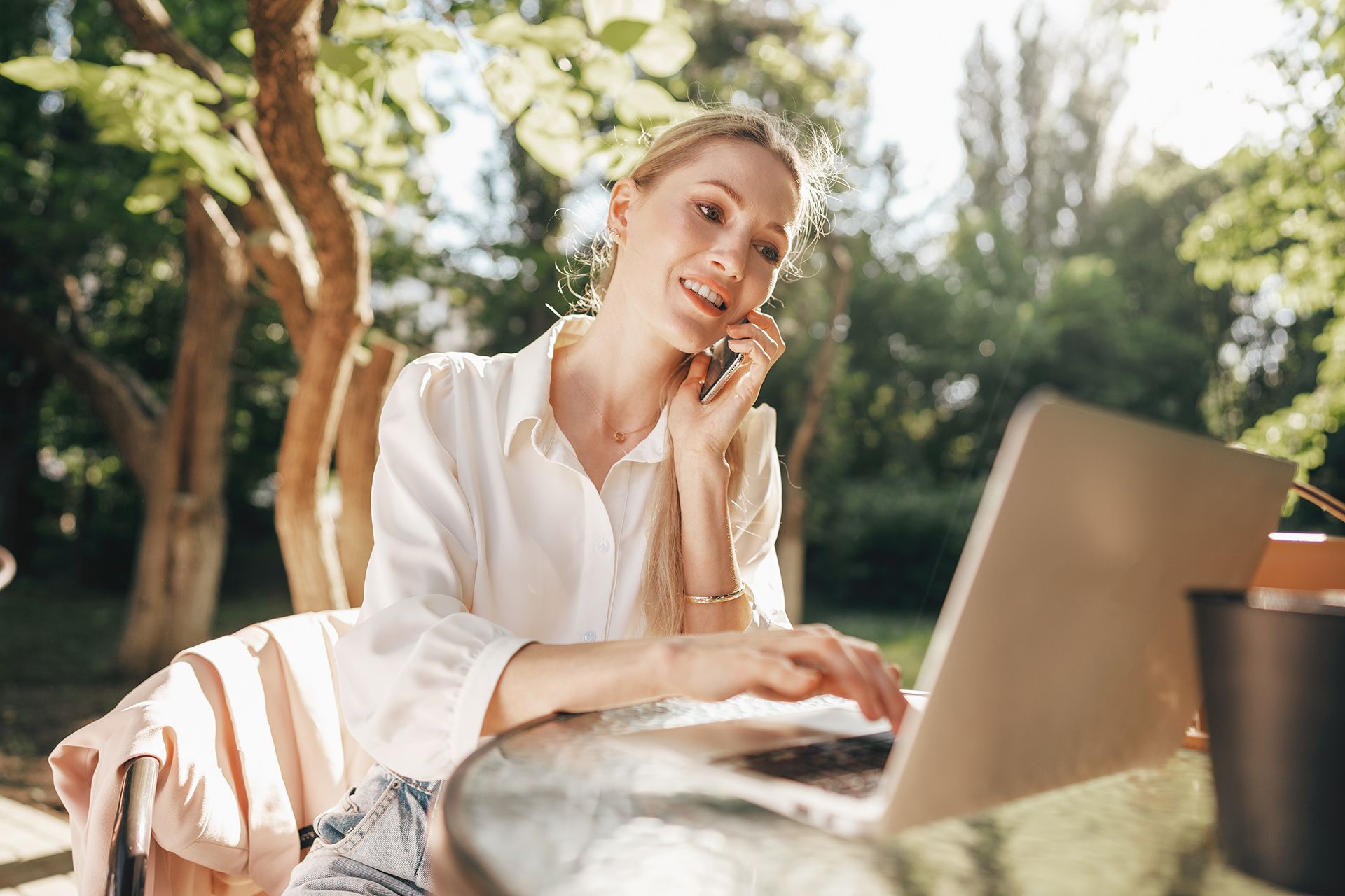 a woman is sitting at a table with a laptop and talking on a cell phone .