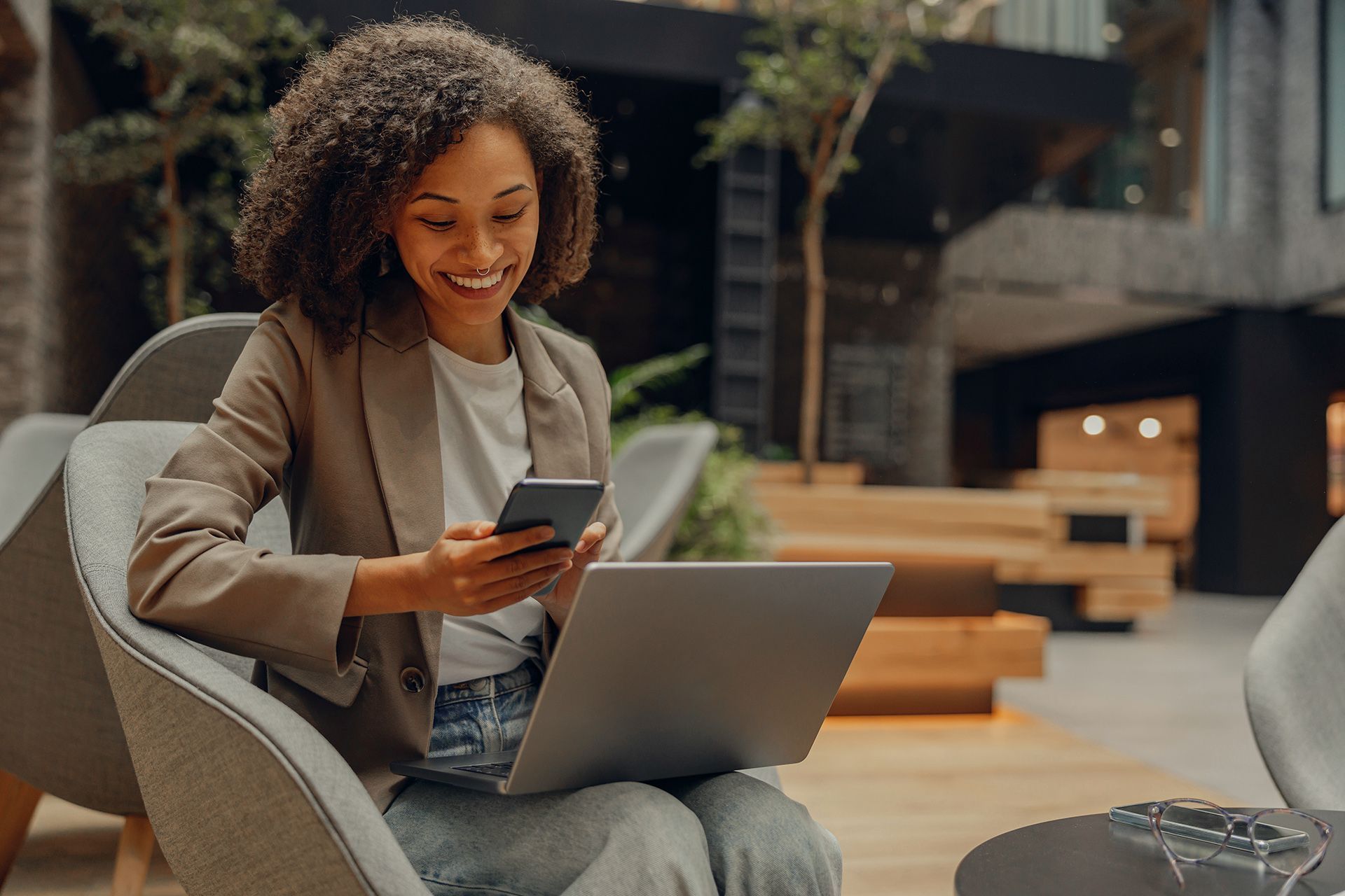 a woman is sitting in a chair using a laptop and a cell phone .