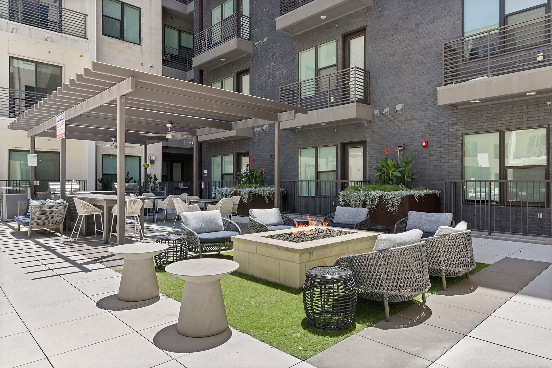 Apartment courtyard with outdoor seating, fire pit, and pergola beside modern building.