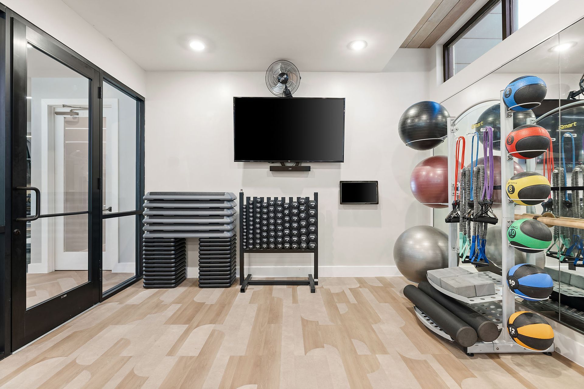 Modern fitness room with a wall TV, stacked step platforms, a treadmill, and exercise balls on a rack.