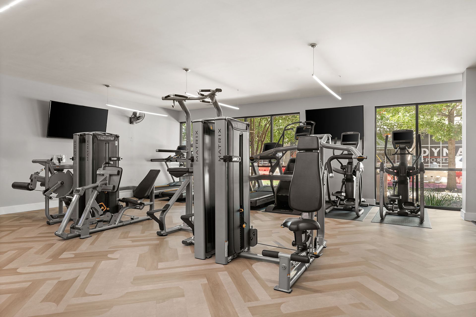 Modern home gym with exercise machines, mirrored walls, wood floors, and large windows at The Clark.