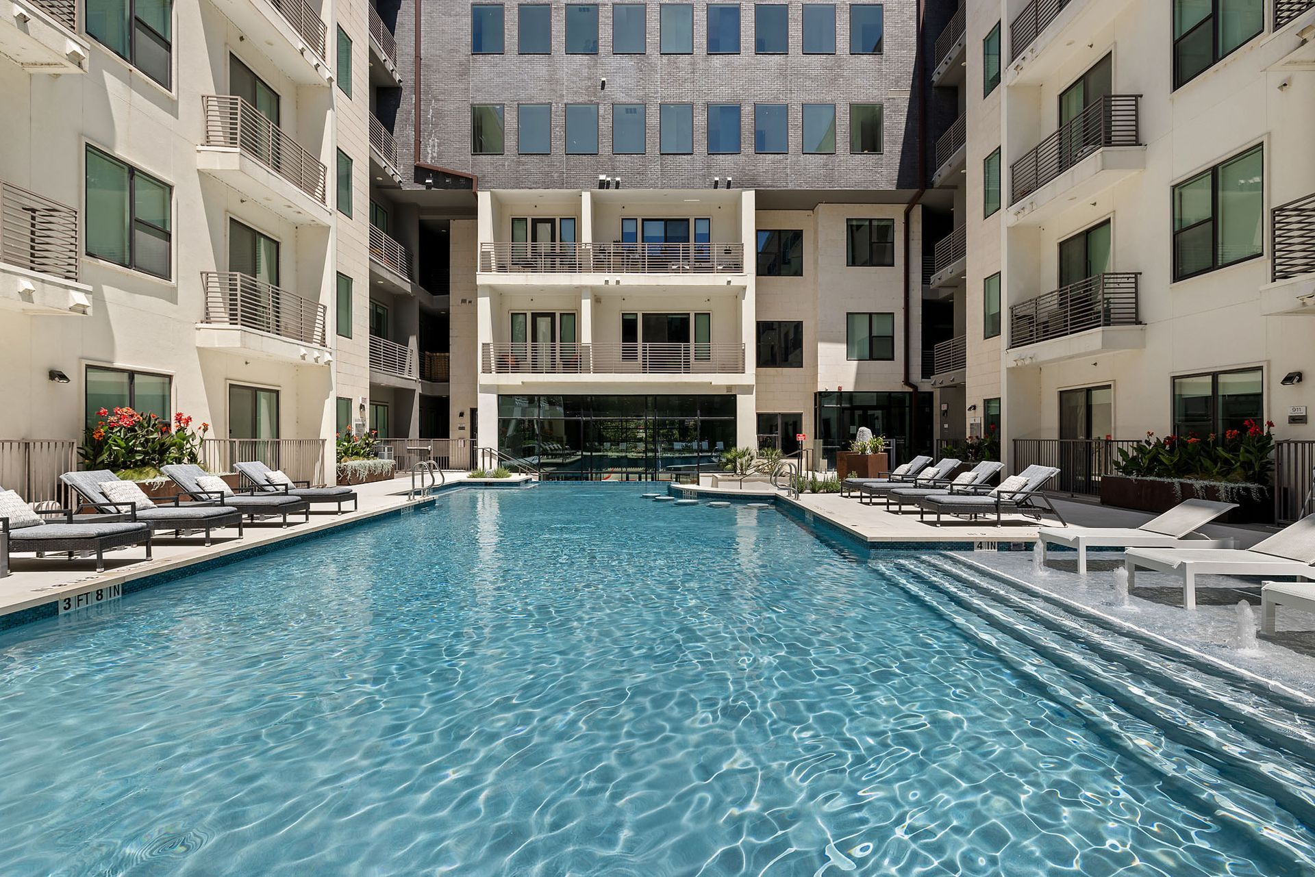 Modern apartment courtyard with a long turquoise swimming pool and lounge chairs on both sides