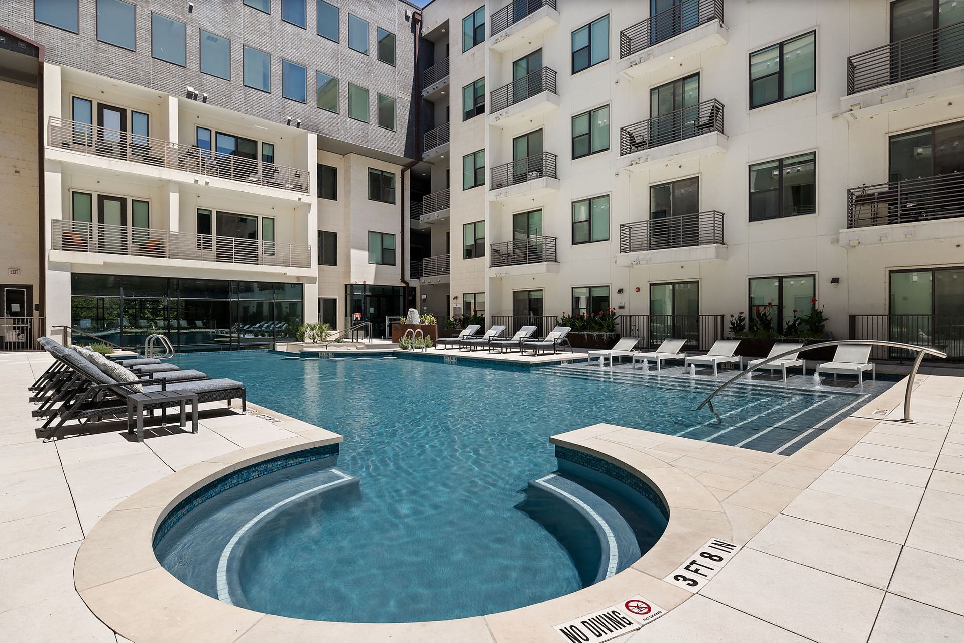 Modern apartment courtyard with a blue swimming pool and lounge chairs in bright sunlight