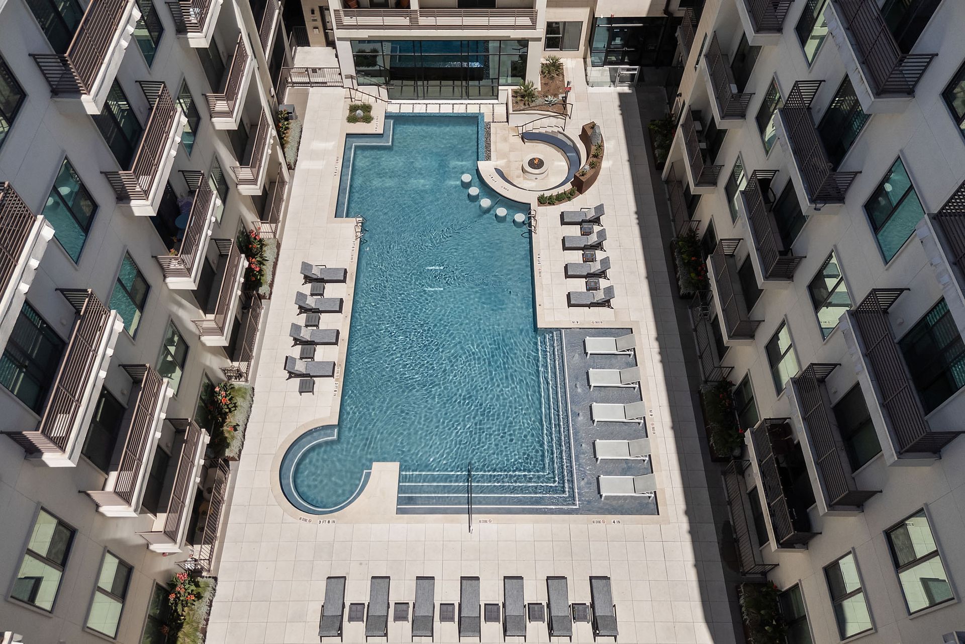Courtyard pool with lounge chairs between apartment buildings, viewed from above.
