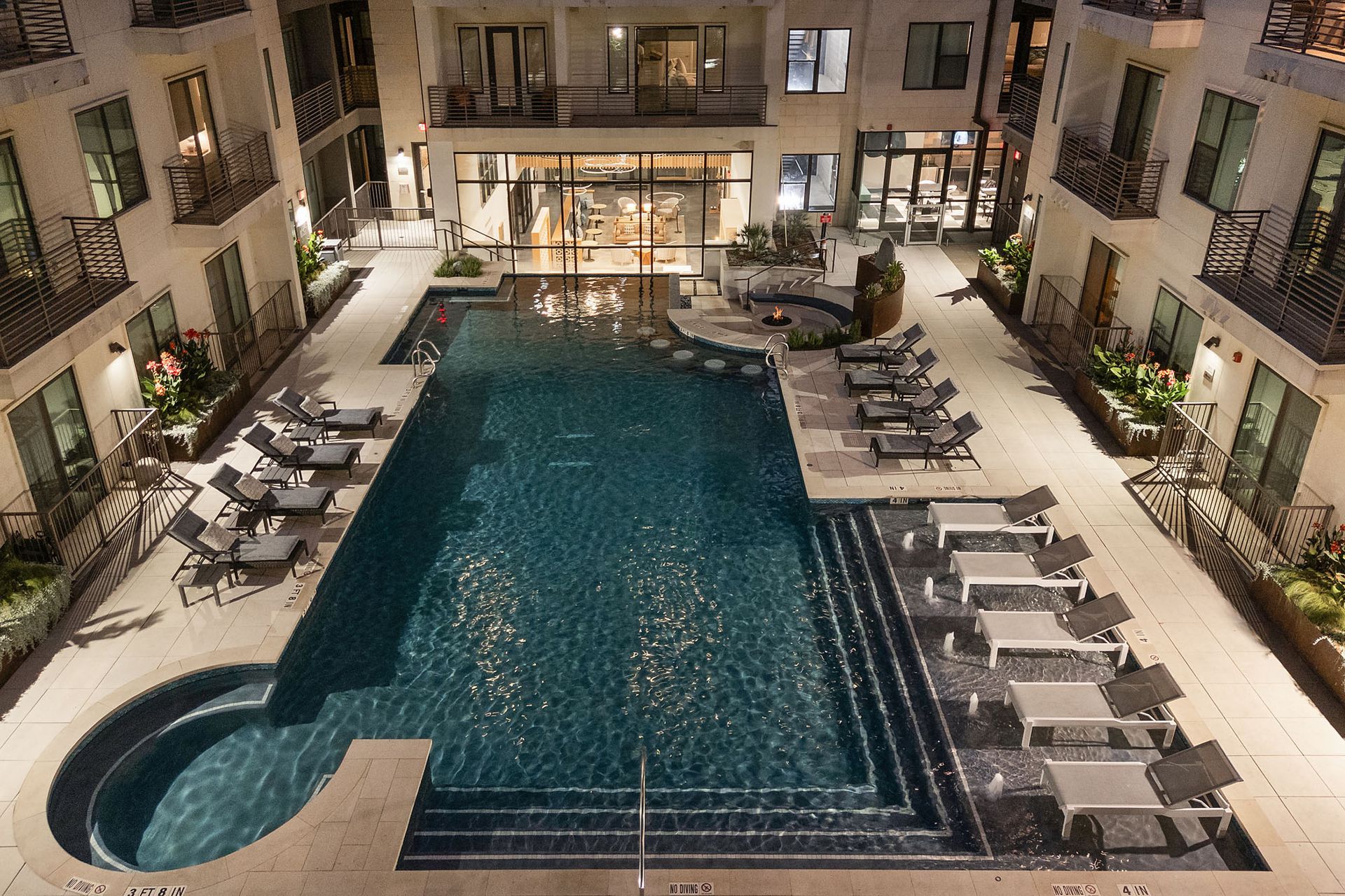 Courtyard hotel pool at night, with lounge chairs and lit balconies surrounding a rectangular pool.